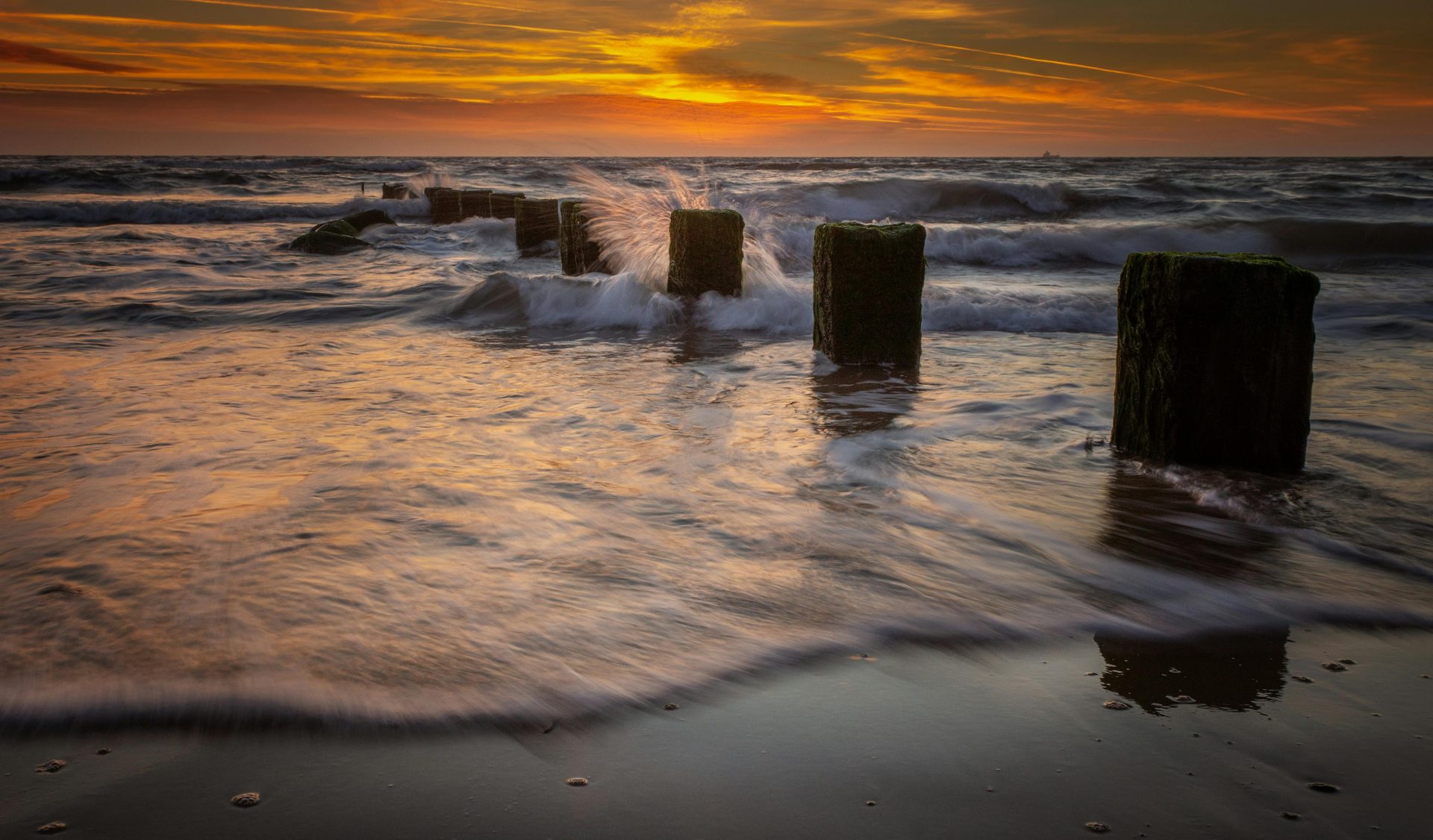 Dramatic sunset over a serene ocean with waves crashing against a wooden jetty.