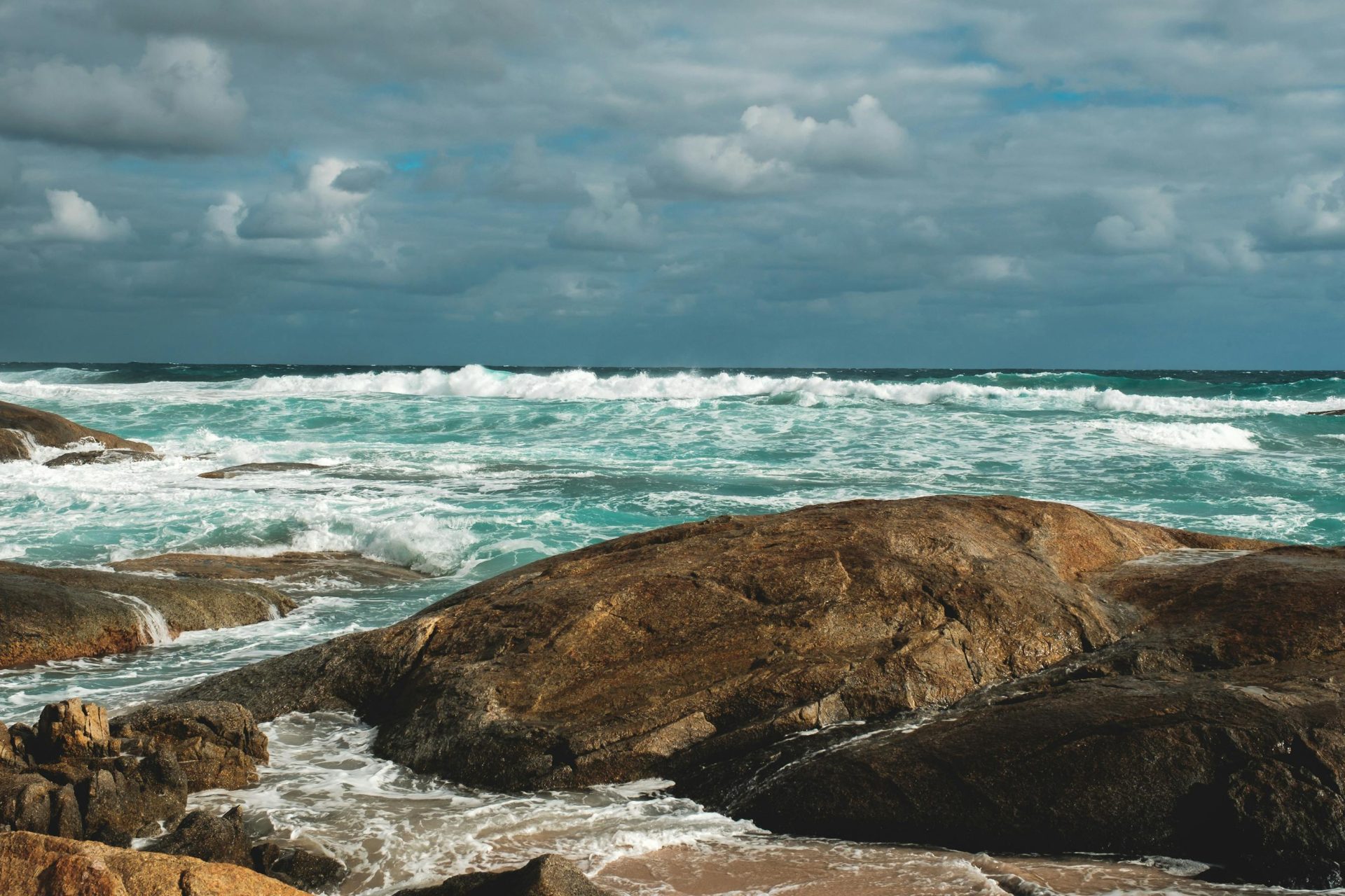 Scenic view of turquoise sea with foamy waves rolling on rough stony shore on cloudy day